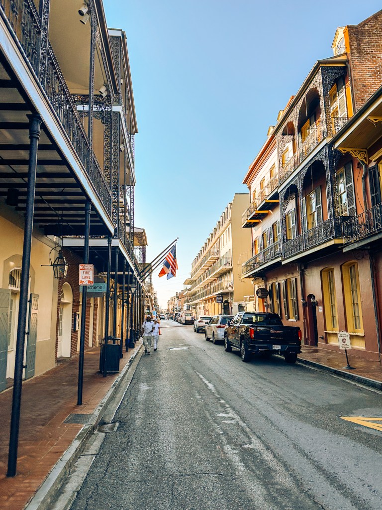 Iconic French Quarter street in New Orleans at sunrise – colorful Creole townhouses with famous wrought-iron balconies, American flags, and empty cobblestone street in soft morning light